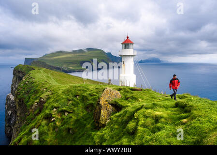 Mykinesholm islet lighthouse near Mykines island. Mykinesholmur, Faroe islands. Tourist in red jacket explores attractions. Summer landscape Stock Photo