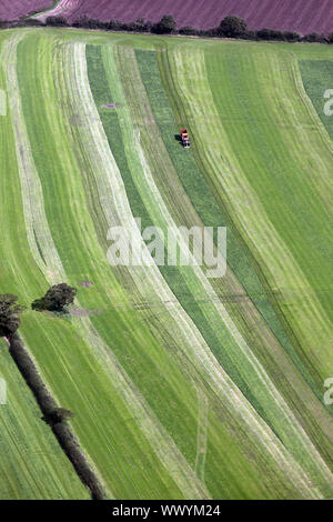 aerial view of a tractor cutting a grass field for hay and leaving stripes of cut and dried grass, Cheshire, UK Stock Photo