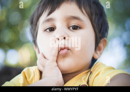 Sad, Brunette boy putting funny faces in an outdoor park Stock Photo