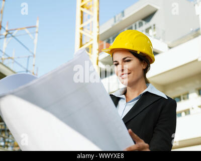 female engineer looking at blueprints in construction site Stock Photo