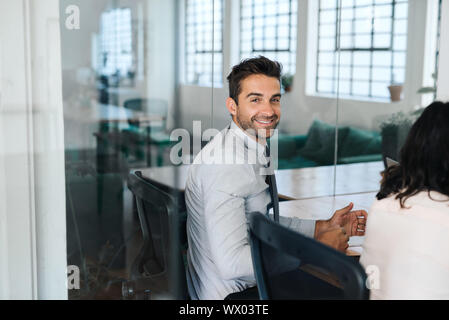 Smiling young businessman sitting with colleagues in a boardroom Stock Photo
