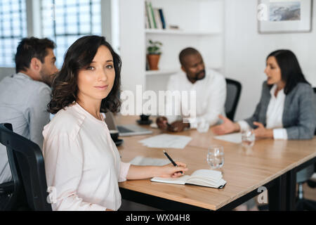 Smiling young businesswoman sitting with colleagues in a boardroom Stock Photo