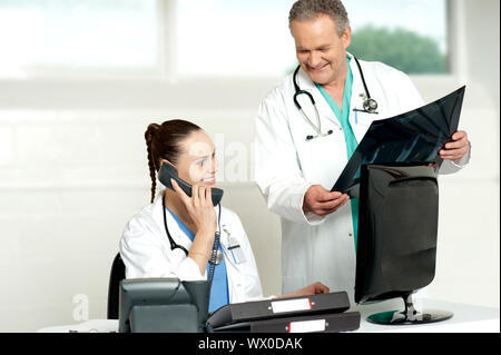 Doctors team in a lab discussing x-ray report. Woman on a call and man showing x-ray report to woman Stock Photo