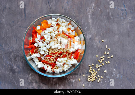 Salad slicing of red and yellow sweet peppers, tomatoes sprinkled with pine nuts and cubes of feta cheese in a glass salad bowl on a vintage shabby ba Stock Photo