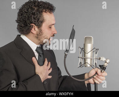 portrait of young man in suit singing with the studio microphone. Isolated on grey background. Singer concept. Stock Photo