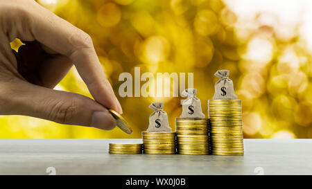 Making money and money investment, Savings concept. A man hand on rising stack of coins with money bag and golden background. Depicts long-term invest Stock Photo