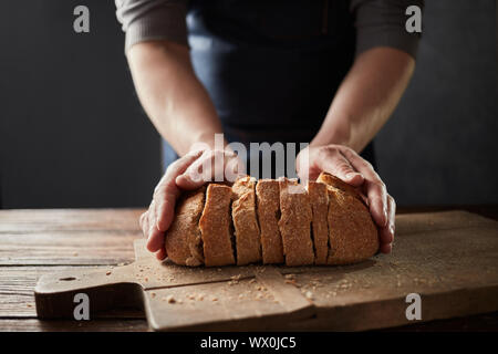 Fresh home slice bread in male's hands on the wooden board. Stock Photo