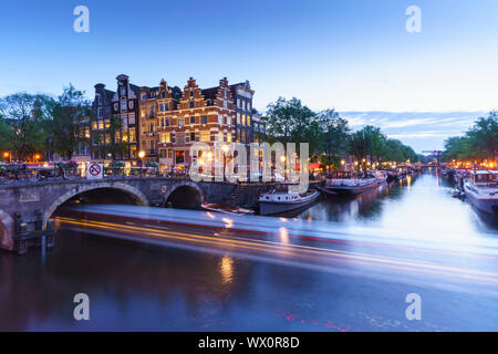 Dusk on Brouwersgracht Canal with trailing light from a tourist boat passing under a bridge, Amsterdam, North Holland, The Netherlands, Europe