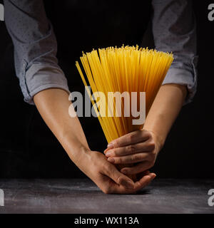 view bunch of raw spaghetti in female hands on black wood vintage table Stock Photo