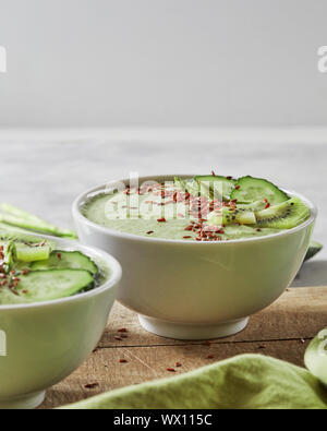 Green smoothies with a cucumber, kiwi and flax seeds in a plate on an old wooden board. Vegetarian food Stock Photo