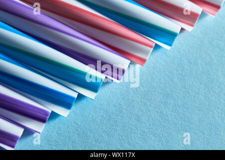 Striped drink straws of different colors in row isolated on blue background Stock Photo