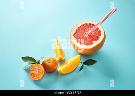Orange and mandarin slice with halves grapefruit and red straw on blue background Stock Photo