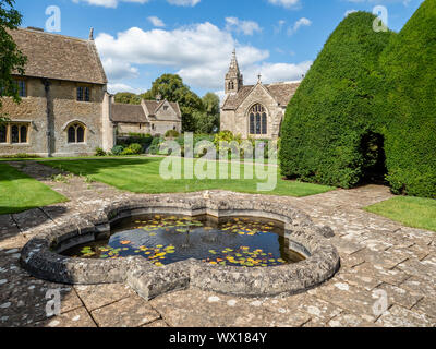 Great Chalfield Manor in Wiltshire UK - ornamental pond and yew castle in the garden with church beyond Stock Photo