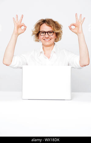 Corporate lady showing excellent gesture to camera sitting in front of laptop Stock Photo