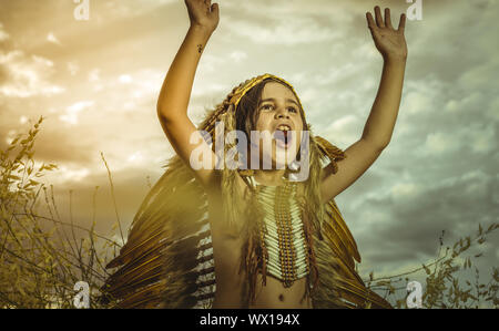 West, American Indian boy dressed in traditional feathered costume, wearing a tuft on his head, picture at sunset in a wheat fie Stock Photo