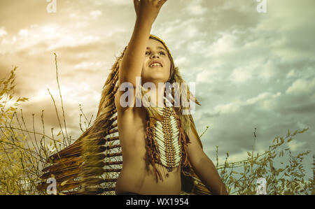 West, American Indian boy dressed in traditional feathered costume, wearing a tuft on his head, picture at sunset in a wheat fie Stock Photo