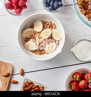 Healthy breakfast ingredients on a white woodwn background. Granola, nuts, berries, milk, banana in bowl , top view Stock Photo