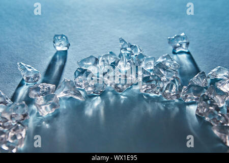 Pieces of crushed ice cubes in the in the form of an arc with long shadows and reflections on the surface on a blue background w Stock Photo