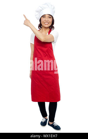 Beautiful female chef pointing at the copy space. Full length shot Stock Photo