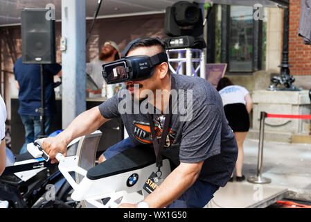 A man wearing virtual reality goggles and riding a motorcycle simulator Stock Photo