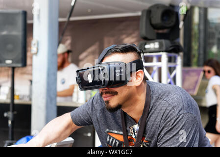 A man wearing virtual reality goggles and riding a motorcycle simulator Stock Photo