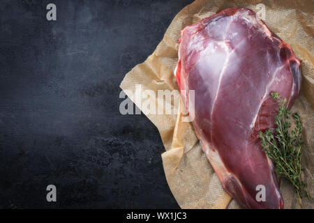 Raw aged leg of venison with bone and thyme as top view on brown paper with copy space left Stock Photo