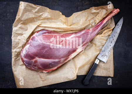 Raw aged leg of venison with bone as top view on brown paper Stock Photo