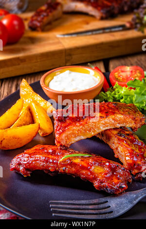 bbq spareribs on the plate with green salad and white sauce. Stock Photo