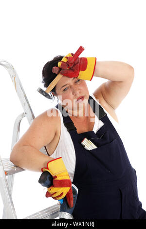 Exhausted DIY housewife or artisan wearing dungarees and safety gloves leaning against her ladder with a tired expression clutching her tools Stock Photo