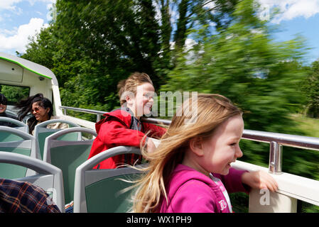 Two children laughing with wind in their faces on an open top double decker bus in the Lake Distrcit, Cumbria, UK Stock Photo