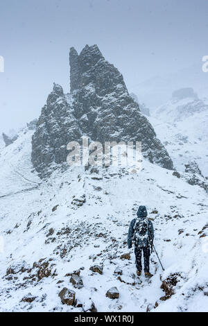 A walker approaching a rock pinnacle in a heavy snow shower, near the Old Man of Storr, Isle of Skye, Scotland, UK Stock Photo