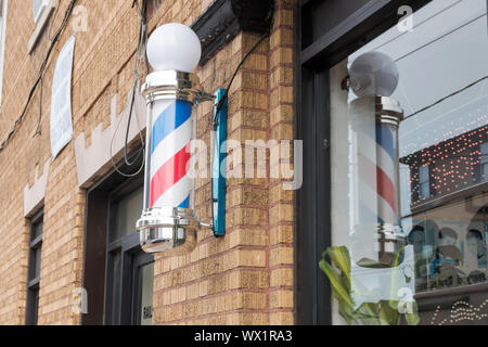 An old fashion Barber Shop Pole on the side of a brown brick building and a reflection of the pole in the window Stock Photo