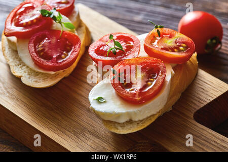 Italian tomato bruschetta with chopped vegetables, mozzarella, herbs and crusty ciabatta bread on a wooden board. Stock Photo