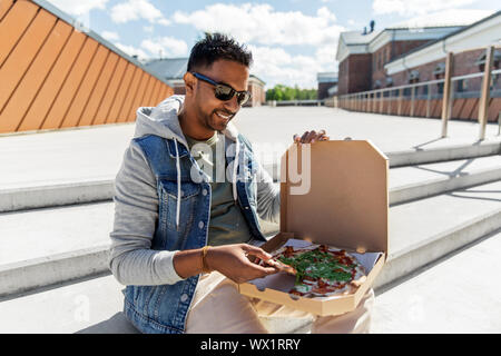 indian man eating takeaway pizza on roof top Stock Photo