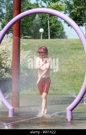 A young boy (7 yrs old) grimaces as he passes through water spray in a water park Stock Photo