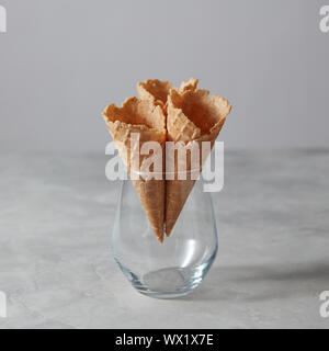 Three empty wafer cones in a glass vase standing on a gray stone table. Stock Photo