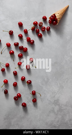 Summer colorful pattern of red natural organic fruit cherry with waffle cone on a gray concrete. Stock Photo