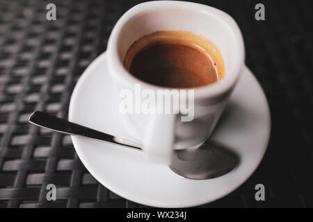 Details with a white ceramic cup of coffee and a stainless steel spoon on a table in a coffee shop Stock Photo