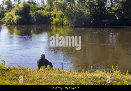 A fisherman on the shore of a small river. Stock Photo
