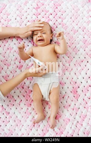 mother measuring temperature of crying baby Stock Photo