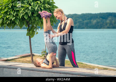 woman and child are training near the lake at the summer park, sporty mother and daughter, fitness and yoga Stock Photo