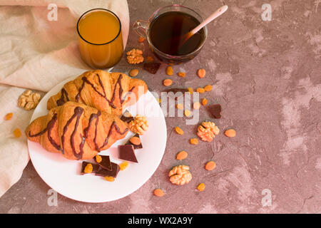 Two chocolate croissants raisins, nuts, a cup of coffee and a glass of orange juice on a gray background. Top view. Breakfast concept. Stock Photo