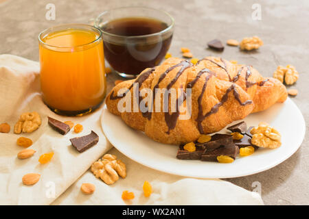 Two chocolate croissants raisins, nuts, a cup of coffee and a glass of orange juice on a gray background. Close-up. Breakfast concept. Stock Photo