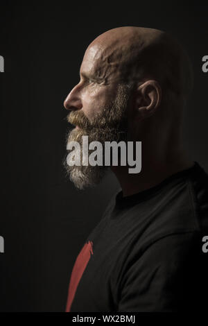 a bearded man with a bald head side view and dark background Stock Photo