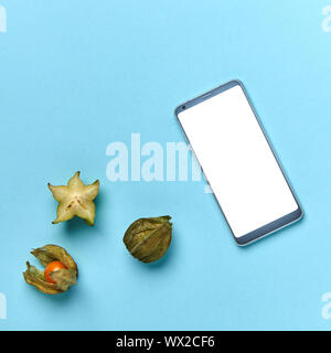 Physalis, a slice of carambola and a mobile phone on a blue background with copy space. The concept of buying products online. F Stock Photo