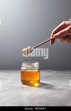 Wooden stick with natural flower honey in a womans hand above a gray concrete table. Rosh hashanah jewish New Year holiday. Stock Photo