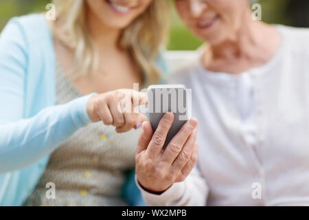 daughter and senior mother with smartphone at park Stock Photo