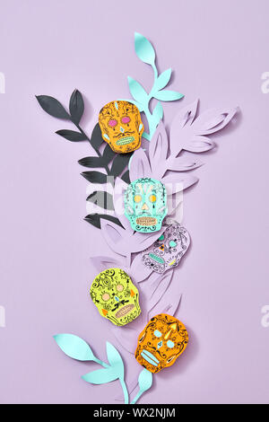 Handmade craft composition of multi-colored paper leaves and Calaveras attribute of the Mexican holiday of Calaca on a purple ba Stock Photo