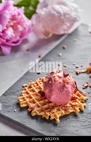 A scoop of berry ice cream on a wafer with chocolate chips on a slate plate on a gray concrete table against a background of pin Stock Photo