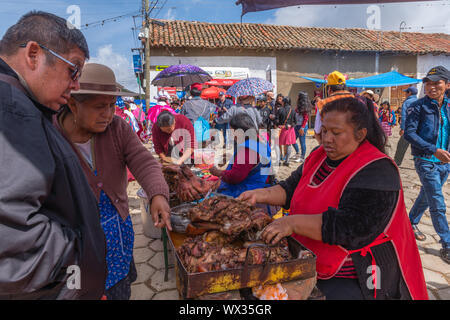 Woman selling fried meat at an open air stall. Very busy Sunday market in Tarabuco, department Sucre, Bolivia, Latin America Stock Photo